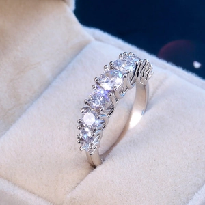 Macro shot of silver wedding ring with five claw-set zircon stones on beige velvet box