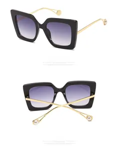 Detail of oversized square sunglasses featuring gold metal temples with pearl tip accents