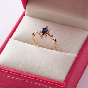 Detail of rose gold ring with marquise blue gemstone and pavé crystals in red box