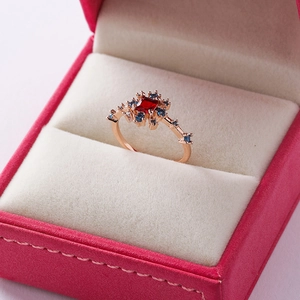 Macro shot of a rose gold ring with a square ruby and tiny blue zircons in a pink gift box