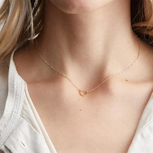 Detail shot of a minimalist gold-plated necklace with a circular pendant on a model's neck