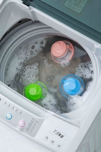 Three floating laundry lint filter bags in pink, blue, and green inside a washing machine