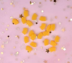 Flat lay of orange resin fan-shaped DIY charms with star sequins on pink background
