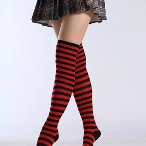 Détail de chaussettes hautes rayées rouge et noir avec une jupe plissée à carreaux