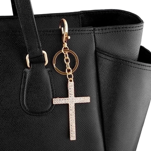 Elegant gold crystal cross keychain with rhinestones attached to a black leather bag