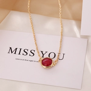 Elegant gold chain necklace with a round deep red gemstone pendant on a display card