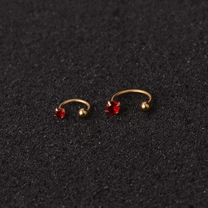 Macro shot of gold C-shaped ear studs featuring red zircon gems and smooth metal ball ends