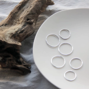 Detailed view of six minimalist silver stacking rings displayed on a white ceramic tray