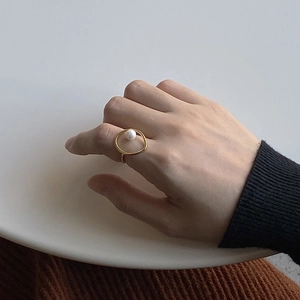 Close-up of a minimalist gold ring featuring a white pearl on a model's hand