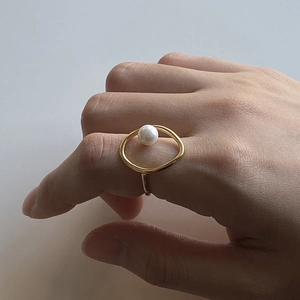 Detail of a minimalist gold ring with an oval cutout and a white round pearl inlay