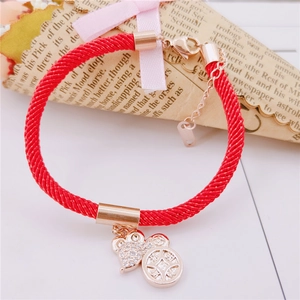 Detail of red woven cord bracelet with rose gold heart charm and coin pendant