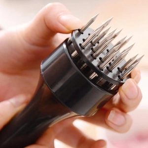 Close-up of hand holding meat tenderizer with sharp stainless steel needles and black handle