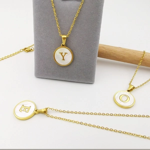 Detailed shot of three gold necklaces with white shell pendants featuring letters Y, E, and O