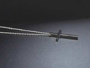 Detailansicht eines polierten Silberkreuz-Anhängers an einer Gliederkette auf grau