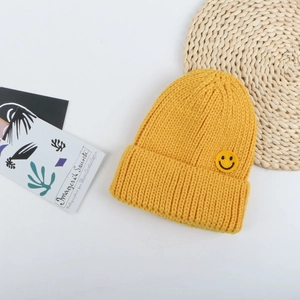 Dettaglio ravvicinato del berretto in maglia gialla con patch smiley su stuoia