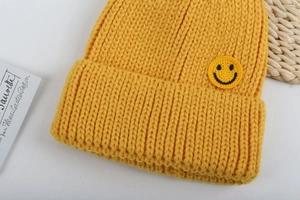 Primo piano del berretto giallo in maglia spessa con toppa ricamata a forma di sorriso