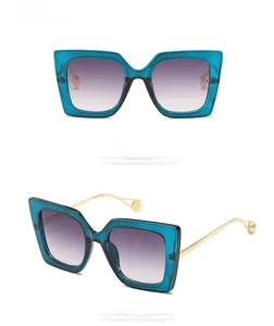 Detail of teal square sunglasses featuring pearl-tipped gold metal temples and gradient lenses