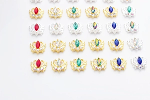 Détail de breloques d'ongles en forme de couronne avec strass colorés sur fond blanc