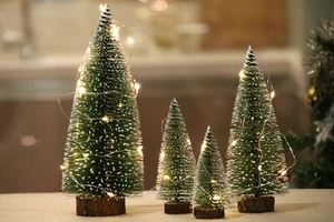 Dettaglio di quattro mini alberi di Natale innevati con luci LED e basi in legno