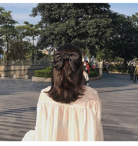 Vue détaillée d'une grande barrette à nœud en satin noir portée dans un parc