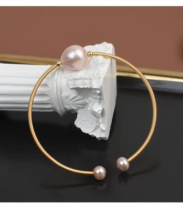Detail of handmade gold wire-wrapped bracelet featuring three pink baroque pearls on a stand