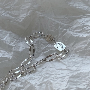 Macro shot of 925 silver bracelet chain with engraved NAU NAU disc and portrait pendant