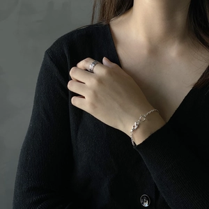 Close-up of silver OT buckle heart bracelet and hollow ring set on a model with black knitwear