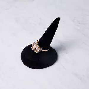 Golden crown ring with white rhinestones on black velvet stand over marble background