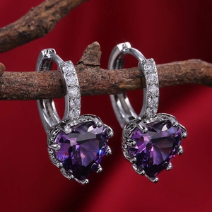 Detailed shot of silver heart earrings with purple crystals on a velvet background