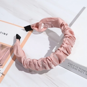 Detail shot of a pink satin pleated headband on a white marble surface with soft lighting