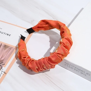 Detail of orange pleated satin headband with golden shimmer on marble surface
