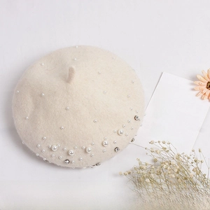 Detail of cream wool beret with hand-sewn pearls and rhinestones on white background