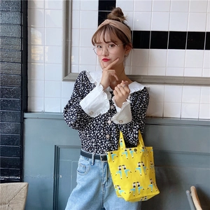 Detail of yellow canvas lunch bag with figure print paired with floral ruffle shirt