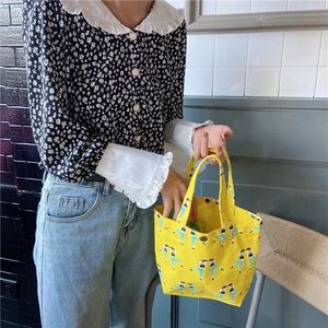 Detail of yellow canvas lunch bag featuring blue figure illustrations and handle texture