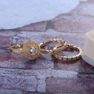 Close-up of three stacked gold-toned geometric rings with sparkling zircon pavé on a stone surface