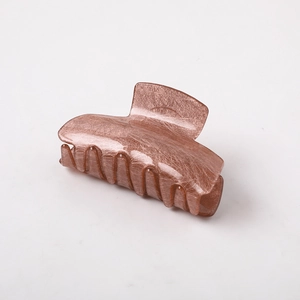 Detail showing brown hair claw clip with brushed metal texture and multi-tooth design