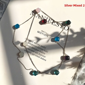 Detail of multi-color gemstone pendants on a silver chain displayed over a magazine