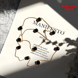 Detail view of a long gold chain necklace featuring faceted black gemstones on a magazine