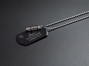 Detail of matte black dog tag with Rambo engraving and polished silver bullet pendant