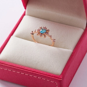 Macro detail of a rose gold flower ring with square blue stone and pink crystals