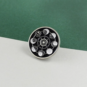 Macro shot of circular enamel moon phase brooch with black and white planetary orbit design