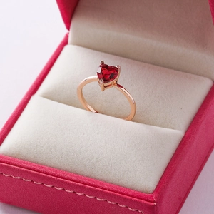 Macro shot of a red heart crystal ring in a rose gold setting inside a pink velvet box