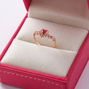Close-up of rose gold flower ring with a red heart-shaped gemstone in a jewelry box