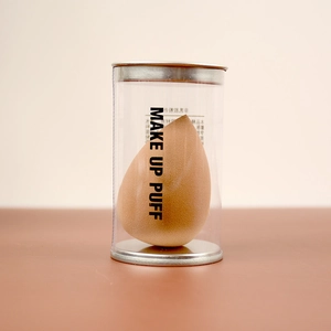 Macro view of teardrop makeup puff in clear cylinder case with silver metallic lids