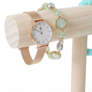 Rose gold mesh watch with green beaded bracelet on solid wood display stand