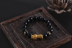 Detailed view of black obsidian beads with gold Pixiu and mantra on wood tray