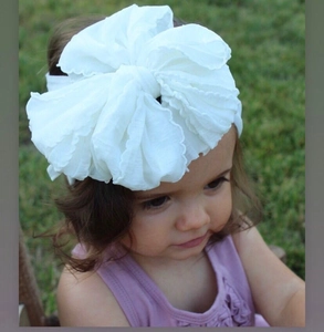Detail of white oversized layered chiffon bow headband for toddlers on green lawn