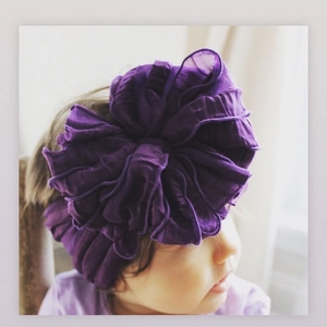 Detail of baby headband with a large dark purple pleated fabric flower and wide elastic band