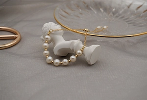 Detail of adjustable gold pearl bracelet elegantly draped on a white plaster sculpture