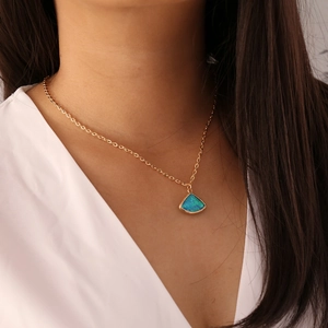 Detalle de collar de cadena dorada con colgante de opalo azul triangular usado por una modelo